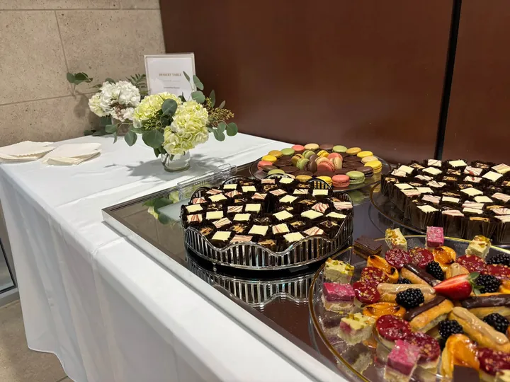 A dessert table with a floral arrangement, petit fours, and macarons at a catered event