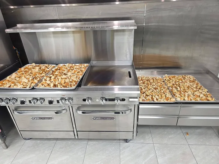 Trays of bread cubes on a commercial kitchen range, prepped for baking