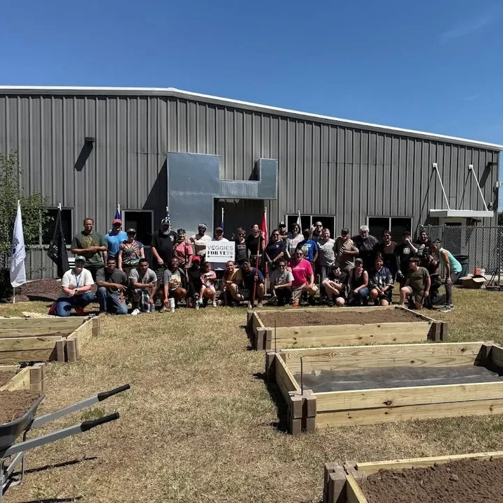 A large group of volunteers gathered behind newly built raised garden beds, with a Veggies for Vets sign