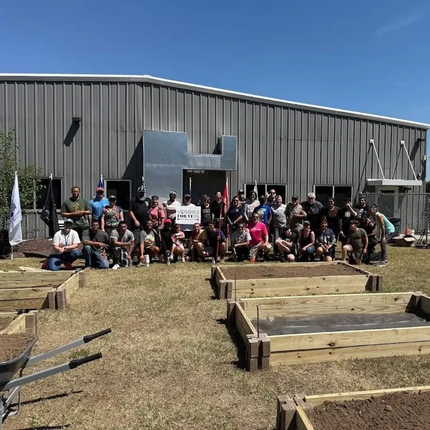 A large group of volunteers gathered behind newly built raised garden beds, with a Veggies for Vets sign